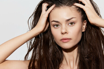 Naklejka premium Portrait of a young woman with wet hair holding her head She has a natural look and emphasizes her striking features against a clean white background Elegant and simple