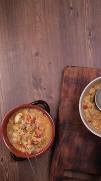 video verticale, uomo che mette pezzetti di pane tostato sulla zuppa, ciotola con zuppa di cicerchie e tagliere con pentola con la zuppa e il mestolo, spazio per testo
