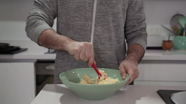 Cooking South American pastries. Closeup view of a man hands blending chipa cheese balls dough with a spatula in the kitchen