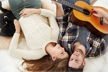 Above, couple and smile on floor with guitar for music notes, bonding and love on break at home. People, relationship and happy or satisfied with instrument for romance, support and trust or care
