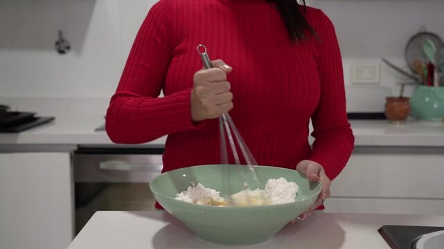 Cooking South American pastries. Closeup view of a woman hands blending chipa cheese balls dough with a whisk in the kitchen