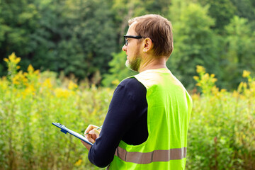 Male ecologist in the forest notes the ecological situation of the environment. Eco technician...