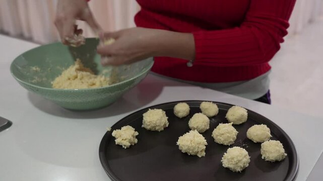 Traditional South American finger food. Closeup view of a woman molding chipa cheese balls with fresh dough, and placing the them in a baking dish