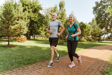 Smiling, happy senior couple running in park wearing sportswear, training together, hobby concept