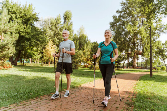 Happy senior couple nordic walking in park wearing sportswear, together exercising outdoors