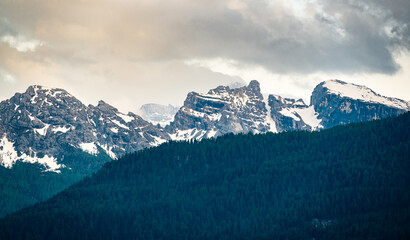 A panoramic view of the Dolomites, with towering mountains and clouds in the background. In the...