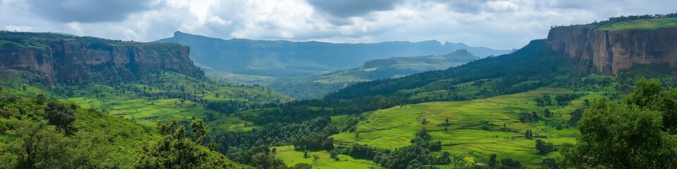 A mountain range with a valley in between. The valley is lush and green. The sky is cloudy and the sun is shining through the clouds