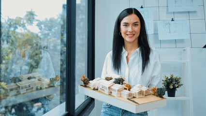 Close up of skilled young beautiful caucasian architect lift house model left side and right sight to check and focus on inspecting mistake point at modern office with blueprint. Immaculate.