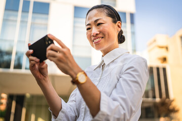 japanese woman play video games on cellphone in front modern buildings