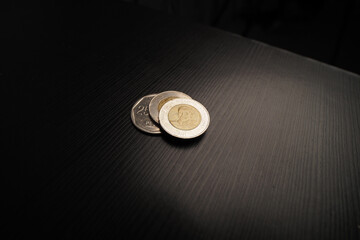 Three coins of Dominican Republic money are placed on a dark wooden table.