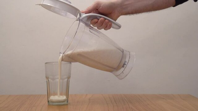 Healthy fitness smoothie. Closeup view of a man pouring a fresh just made banana milkshake with protein, into a glass