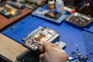 A technician carefully replaces the battery of a phone while working on a repair at a busy workshop in daylight