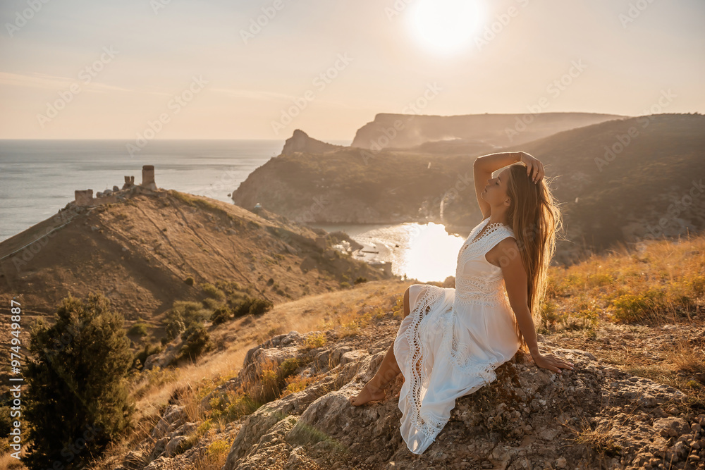 Canvas Prints A woman in a white dress is sitting on a rock overlooking a body of water. She is enjoying the view and taking in the scenery.