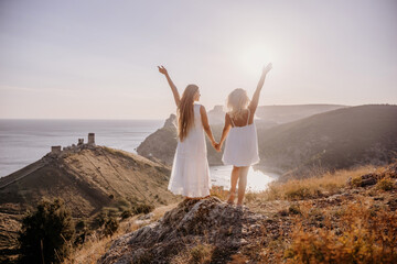 Two women are standing on a hill overlooking the ocean. They are holding hands and looking out at the water. The scene is peaceful and serene, with the sun shining brightly in the background.