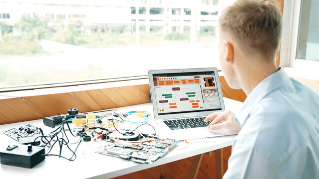 Caucasian student looking at laptop screen while coding engineering prompt or programing system. Back view of smart teenager working by using computer and electronic tool at STEM class. Edification.