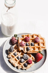 Waffles with fresh berries and a bottle of milk on a white background