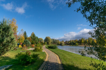 A beautiful park with a pond on a clear day in early autumn. A picturesque landscape with a .paved path for walking along the pond.