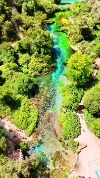 River with turquoise water flowing in the rocky area. Aerial perspective on the mountainous area with lush greenery on sunny day. Vertical video.