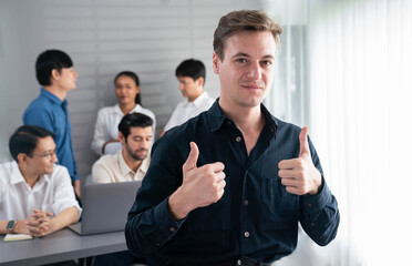 Confidence and happy smiling businessman portrait with background of his colleague and business team working in office. Office worker teamwork and positive workplace concept. Prudent