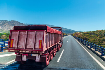Truck with a tipper trailer travelling on a motorway transporting iron ore, the truck is covered in...