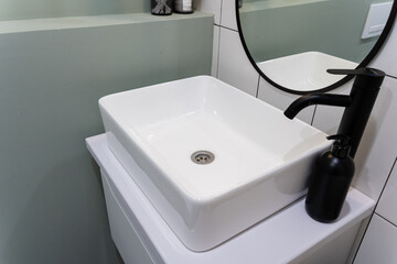Fototapeta premium In a bathroom, there is a sink equipped with a stylish black faucet, complemented by a mirror that adds depth and reflection to the space, creating a functional and aesthetic area