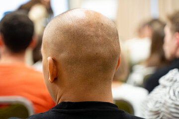 A bald man is sitting quietly in a classroom filled with other people