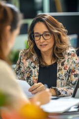 A middle-aged Hispanic businesswoman in a wheelchair happily working on reports with a female coworker in a vibrant office environment..jpg