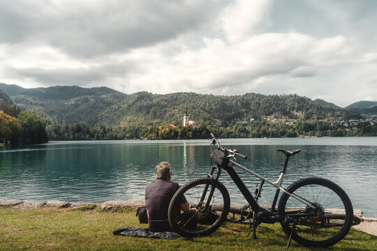 Mann macht nach Radtour eine Pause mit Blick auf Wallfahrtskirche Mari&auml; Himmelfahrt Katholische Kirche auf der kleinen Insel am Bleder See in Slowenien 