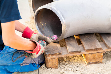 A worker grinds the edge of a weld seam for subsequent welding of a pipe