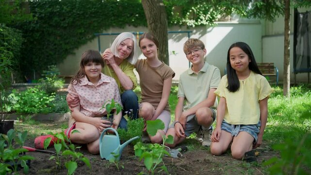 Students and female teacher at outdoor sustainable education class. Kids taking care of plants in school garden. Concept of experiential learning and ecoliteracy.