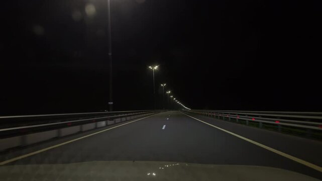 Pov of a driver driving a white car on a night highway with left-hand traffic. The car is being rebuilt from the left lane to the right lane on the highway expressway at night.