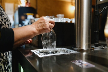 The hands of an elderly woman rinses a glass of beer.