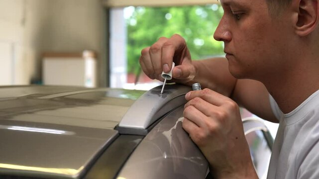 Closeup side view of focused experienced technician male expertly repairing scratches on car roof rack in auto shop, demonstrating proficiency in auto maintenance. Shooting in slow motion.