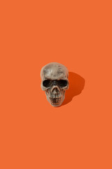 Human skull on orange background. Minimal Halloween idea.
