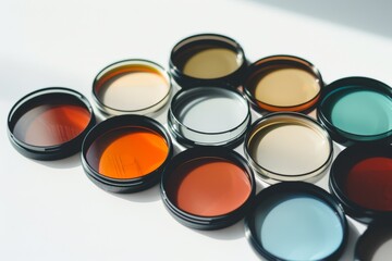 Various camera lens filters in warm, natural light are arranged on a white surface, showcasing a spectrum of colors.