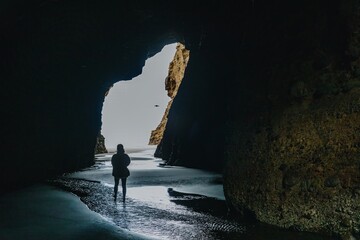 Woman walking through a keyhole hole in the rock cave in Piha, Auckland, New Zealand.