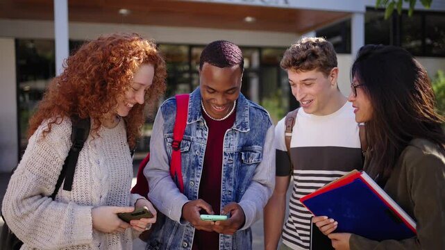 Group diverse genders and races students gathered sharing fun things with mobile phone in campus university. Joyful friends using and looking cell while talking happy about watching on device screen - Powered by Adobe