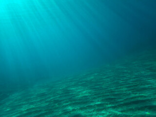 Dark blue ocean surface seen from underwater. Abstract waves underwater and rays of sunlight shining through, Sun light rays undersea deep, Underwater background with sea bottom, Mediterranean sea.