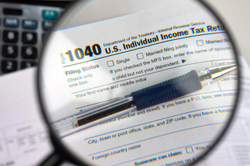 USA personal income tax return. Form 1040 under magnifying glass. Tax papers and calculator....