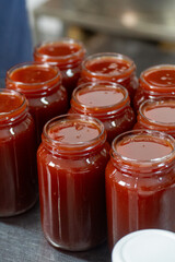Jars of freshly made rosehip jam in an artisan factory. The jam, rich in color and texture, fills the glass jars to the brim, ready for sealing. Captured during production