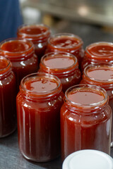 Jars of freshly made rosehip jam in an artisan factory. The jam, rich in color and texture, fills the glass jars to the brim, ready for sealing. Captured during production