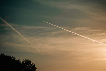A summer sunset gradient with soft clouds and bright jet trails
