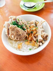 a bowl of meatball noodles mixed with vermicelli, large beef tendon meatballs, chicken feet and caosin vegetables