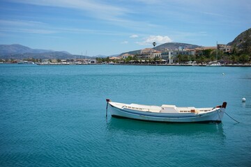 Fototapeta premium small white boat anchored in a bay with turquoise blue water in nafplio in greece on a sunny summer day
