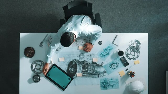 Top down view of skilled engineer writing and planning turbine engine design while sitting at meeting table with gear and electronic generator scatter around. Technician taking a note. Alimentation.