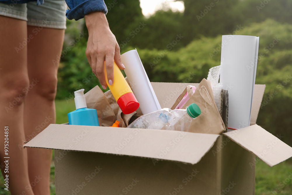 Wall mural Recycling concept. Woman putting plastic bottle into cardboard box outdoors, closeup