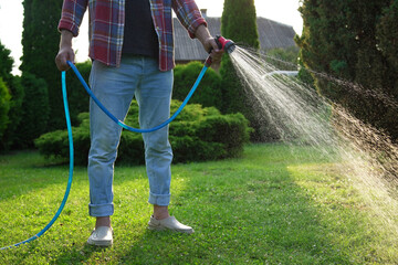 Man watering green grass on lawn in backyard, closeup