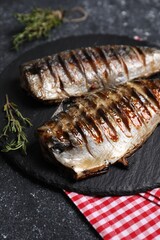 Delicious grilled mackerel, thyme and napkin on dark textured table, closeup