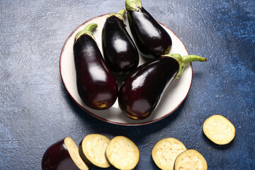 Plate with fresh eggplants on blue background
