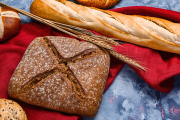 Fresh loaf of rye bread and wheat ears on grey table